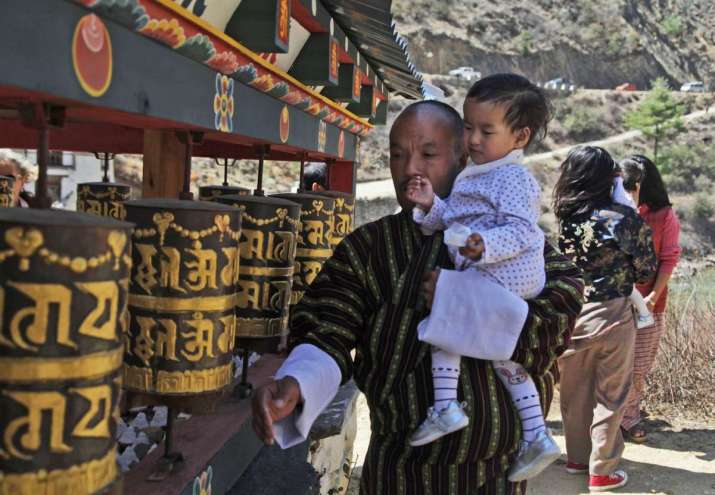Sonam Tshering holds one of his twin daughters as he spins prayer wheels at Tachog Lhakhang. From sbs.com.au