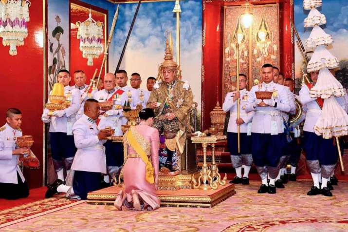 Queen Suthida kneels before King Maha Vajiralongkorn, dressed in full royal regalia. From theguardian.com