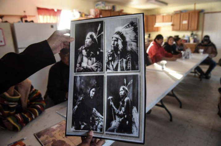 Descendants of those killed at Wounded Knee gather in a community building while a person holds photos of some of their ancestors. From postguam.com